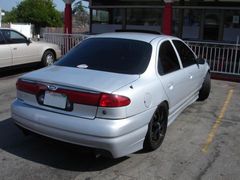 1993 Ford Taurus - A silver sedan is parked in a lot next to another vehicle.