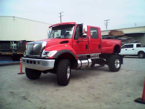 1999 Ford F-800 - Three-quarter front view of a red International crew-cab medium-duty 4x4 pickup on a paved industrial lot, with a chrome bumper and grille,…