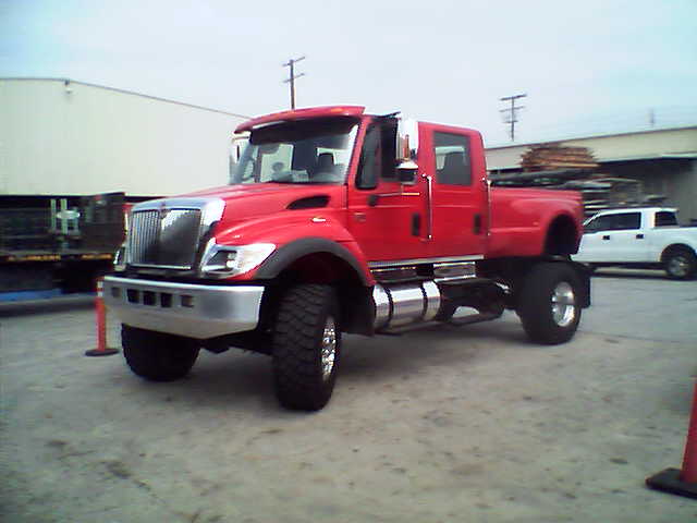 Red International crew-cab 4x4 dually pickup with chrome stacks on an industrial lot