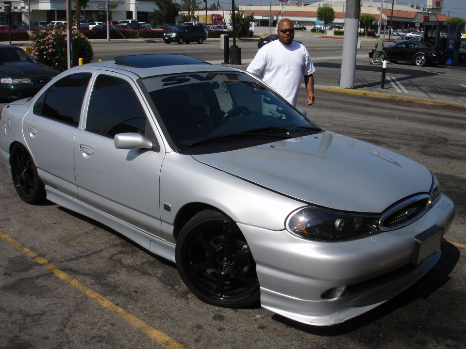 Silver sedan with SVT banner on windshield, aftermarket body kit, and black wheels parked in a lot