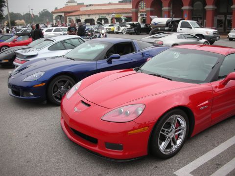 1998 Ford Crown Victoria - A red Chevrolet Corvette is parked in front of a blue Corvette at a car meet.