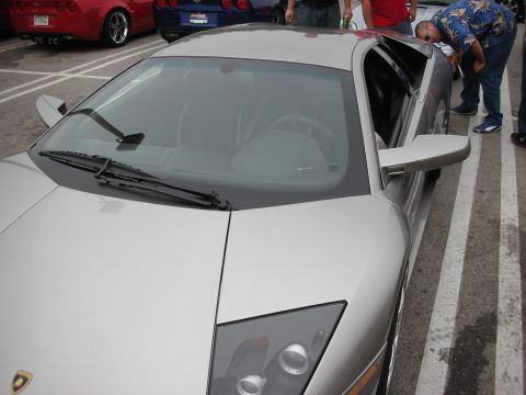 1998 Ford Crown Victoria - A silver sports car is parked in a lot, with other vehicles and people visible in the background.