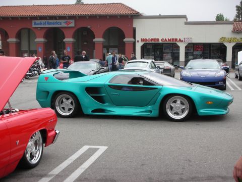 1998 Ford Crown Victoria - A striking teal sports car is parked in a lot, with other vehicles and businesses visible in the background.