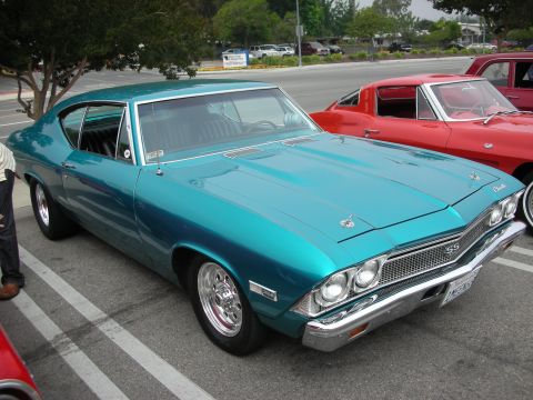 1998 Ford Crown Victoria - A teal 1969 Chevrolet Chevelle SS is parked in a lot next to a red vehicle.