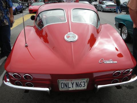 1998 Ford Crown Victoria - A classic red 1963 Corvette Sting Ray is seen from the rear at a car meet, with other vehicles visible in the background.