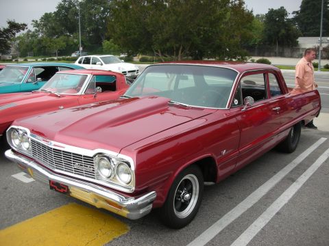 1998 Ford Crown Victoria - A red 1964 Chevrolet Impala sedan is parked next to other classic cars.
