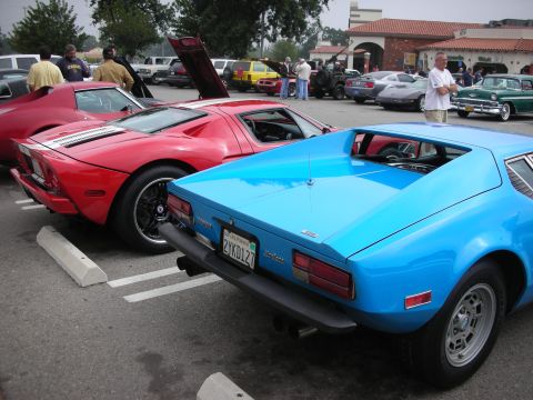 1998 Ford Crown Victoria - A blue sports car is parked in a lot with other vehicles, including a red sports car with its hood open.