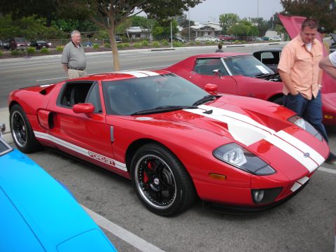 1998 Ford Crown Victoria - A red Ford GT with white racing stripes is parked next to other vehicles at a car meet.