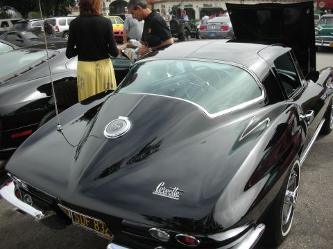 1998 Ford Crown Victoria - A classic black Chevrolet Corvette Sting Ray is parked at an outdoor gathering with other vehicles and people.