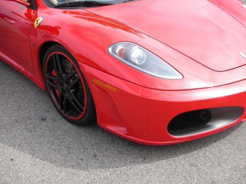 1998 Ford Crown Victoria - Tight three-quarter front detail of a red Ferrari F430 on asphalt, showing the projector headlight, mesh corner air intake, amber side mark…