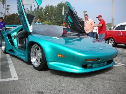 1998 Ford Crown Victoria - A teal sports car with its doors open is parked in a lot next to a red classic car.