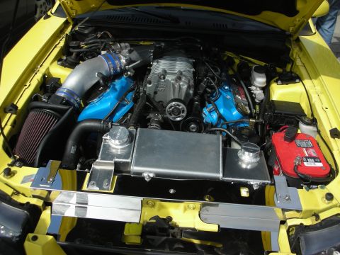 1998 Ford Crown Victoria - The engine bay of a yellow vehicle features a prominent supercharger and custom cooling components.