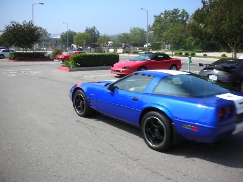 1998 Ford Crown Victoria - A blue Chevrolet Corvette with white racing stripes is parked next to other vehicles.