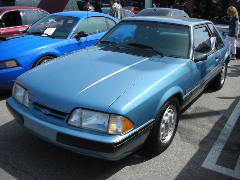 1998 Ford Crown Victoria - A light blue Ford Mustang is parked in a lot with other vehicles.