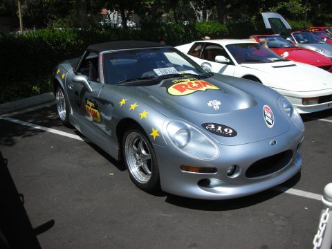 1998 Ford Crown Victoria - A silver convertible sports car with racing decals is parked next to other vehicles.