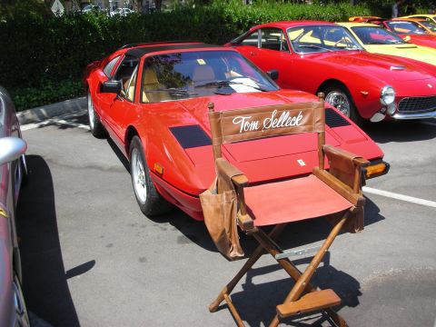 1998 Ford Crown Victoria - A red sports car is parked with a director's chair bearing the name 'Tom Selleck' in front of it, with other classic cars visible in the ba…