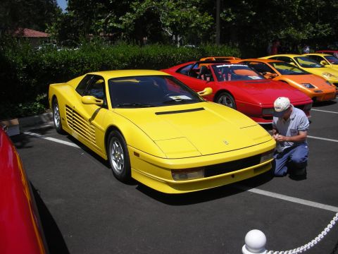1998 Ford Crown Victoria - A man kneels to clean a yellow Ferrari Testarossa, with other exotic cars parked in the background.