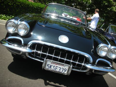 1998 Ford Crown Victoria - A black 1958 Chevrolet Corvette convertible is parked outdoors, with a person standing nearby.