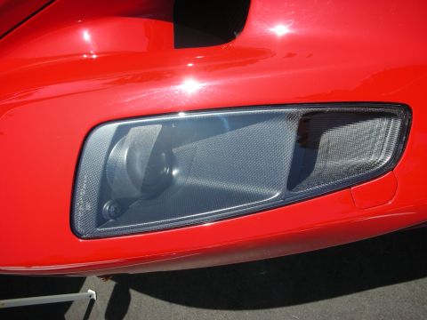 1998 Ford Crown Victoria - The headlight assembly of a red sports car features a carbon fiber textured housing.