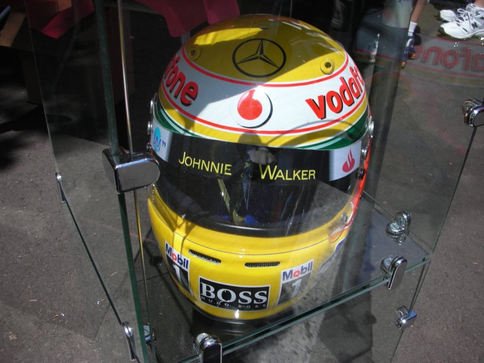 Yellow racing helmet with Vodafone and Johnnie Walker logos, displayed in a glass case
