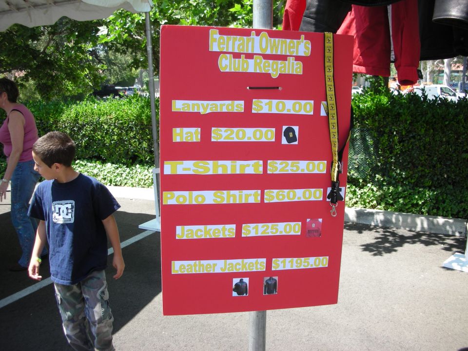 Red Ferrari Owners Club regalia price board listing merchandise prices, photographed at an event