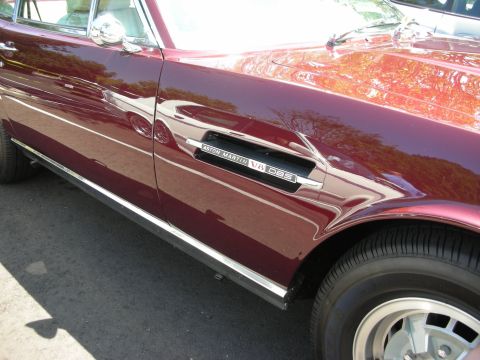 1998 Ford Crown Victoria - Close-up of the side panel on a burgundy Aston Martin V8 DBS, highlighting the chrome trim and fender vent.
