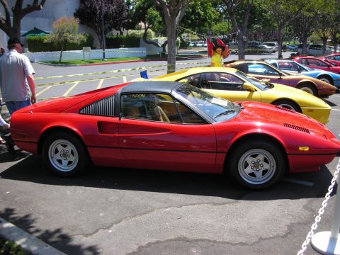 1998 Ford Crown Victoria - A red Ferrari 308 GTS is parked in a lot next to other colorful sports cars.