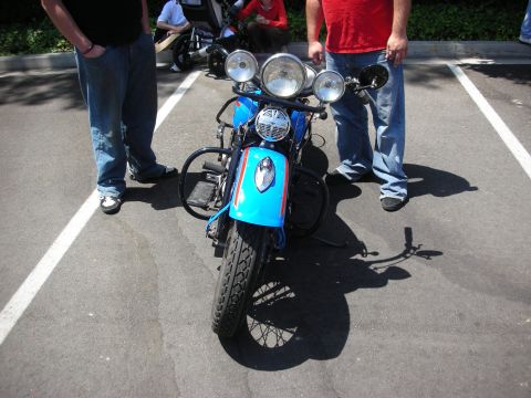 1998 Ford Crown Victoria - A blue motorcycle is parked in a lot, with people standing around it.