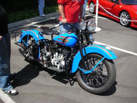 1998 Ford Crown Victoria - A blue vintage motorcycle is parked next to a red sports car.