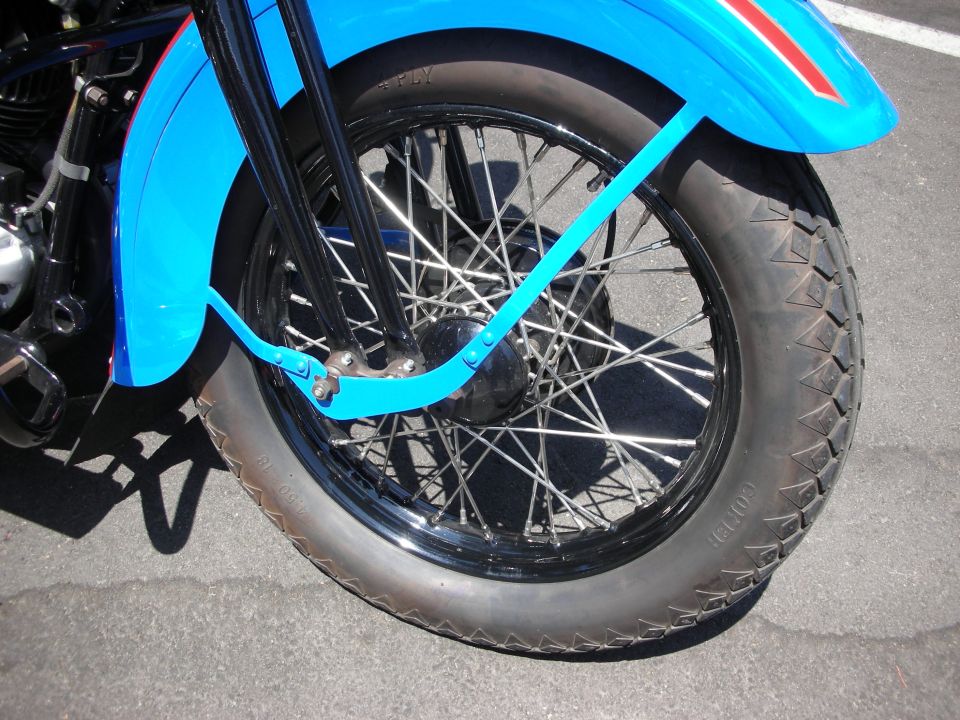 Motorcycle front wheel with spokes, black rim, and blue fender with red stripe