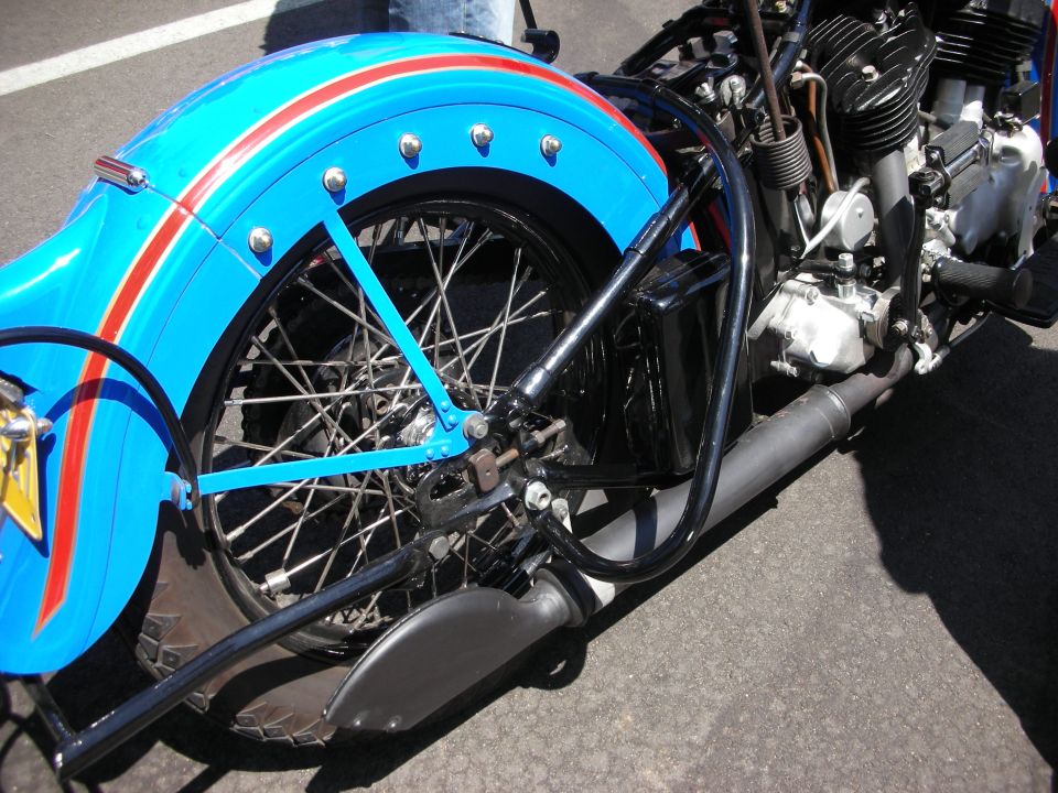 Blue motorcycle rear fender with red stripes and chrome trim, showing spoke wheel and engine detail