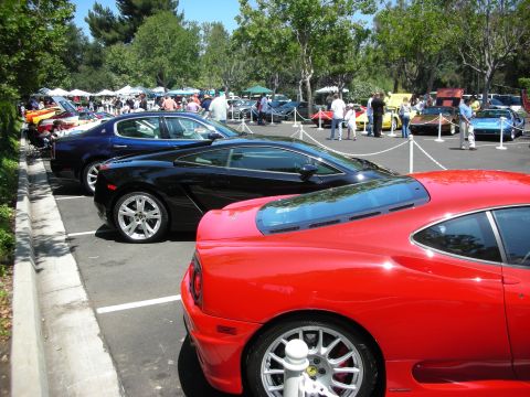 1998 Ford Crown Victoria - Several sports cars are displayed at an outdoor car show with spectators milling around.