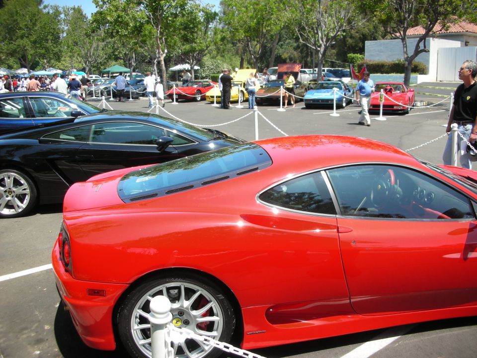 Red sports car parked at an outdoor car show with other vehicles and people around
