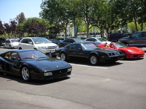 1998 Ford Crown Victoria - A collection of vehicles, including a black Ferrari and a black Pontiac Firebird, are parked in an outdoor lot on a sunny day.