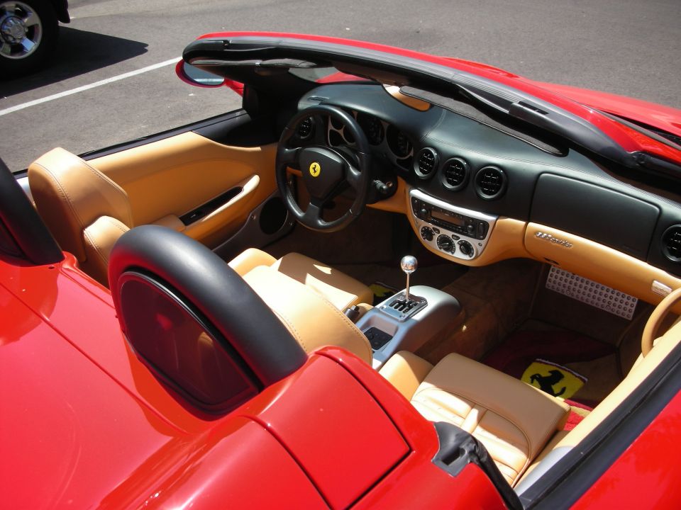 Red convertible interior with tan leather seats, black steering wheel with yellow Ferrari emblem, and silver gear shift