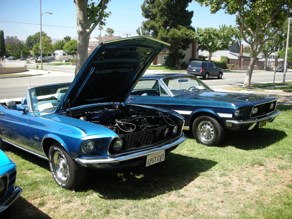 Blue 1969 Mustang convertible with hood open parked next to a dark blue 1969 Mustang coupe