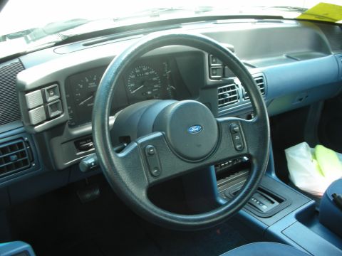 1998 Ford Crown Victoria - The interior of a Ford Mustang, a blue dashboard and seats, with a prominent steering wheel and instrument cluster.
