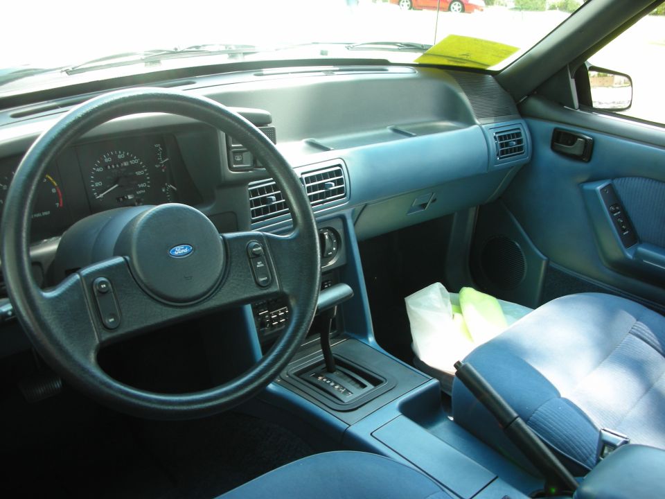 Interior shot of a blue Ford Mustang, showing the steering wheel, dashboard, and seats