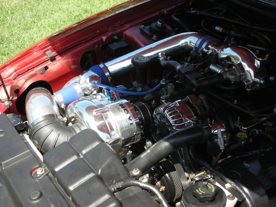 Engine bay with a Novi supercharger, chrome intake piping, and alternator