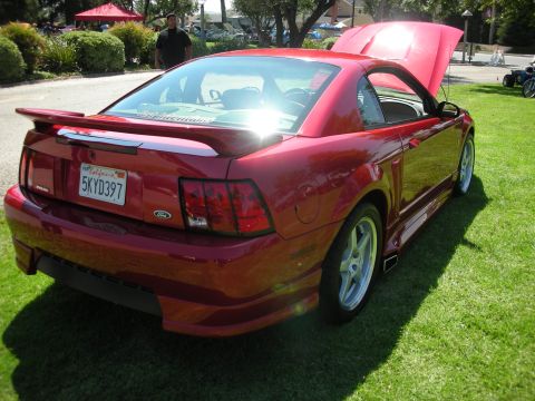 1998 Ford Crown Victoria - A red Ford Mustang is parked on a grassy lawn with its hood open, showing off its engine bay.