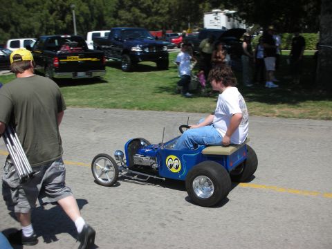 1998 Ford Crown Victoria - A blue go-kart with a driver passes by other vehicles and people at an outdoor event.
