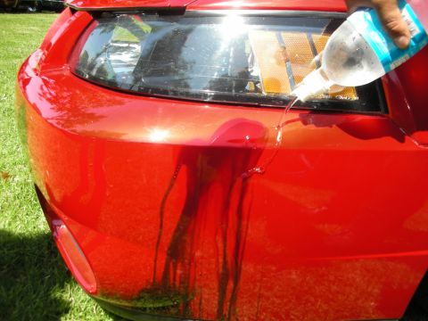 1998 Ford Crown Victoria - Water is poured onto the rear bumper of a red car, causing dark liquid to run down the paint.