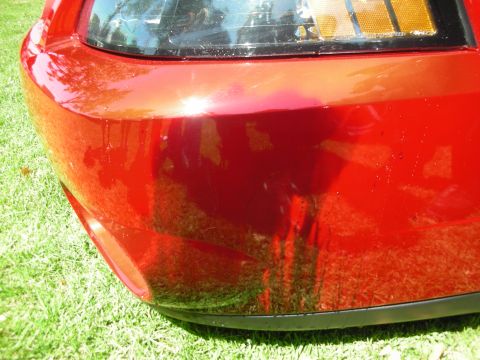 1998 Ford Crown Victoria - A close-up of a red car's bumper shows water droplets on its surface.