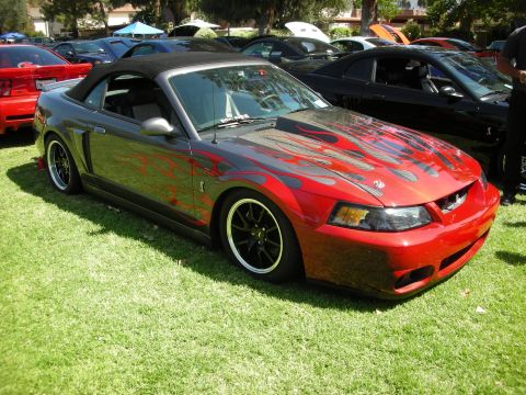 1998 Ford Crown Victoria - A customized convertible Mustang with flame decals is parked on the grass at a car show.