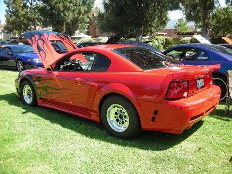 1998 Ford Crown Victoria - Red Ford Mustang with flame decals and drag racing wheels parked on grass at a car show.