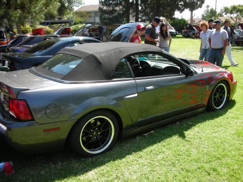 1998 Ford Crown Victoria - A gray convertible Mustang with flame decals is parked on a grassy lawn at an outdoor car show.