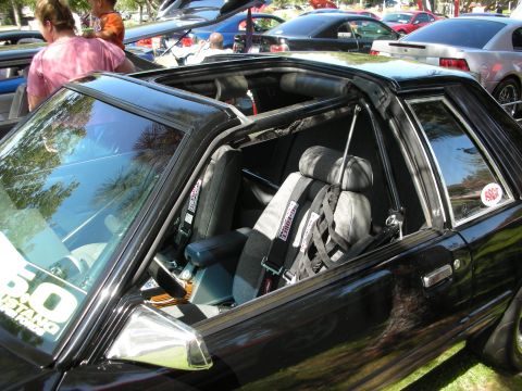 1998 Ford Crown Victoria - The interior of a black Ford Mustang is visible, equipped with racing seats and harnesses, and a "5.0 MUSTANG" sticker on the windshield.