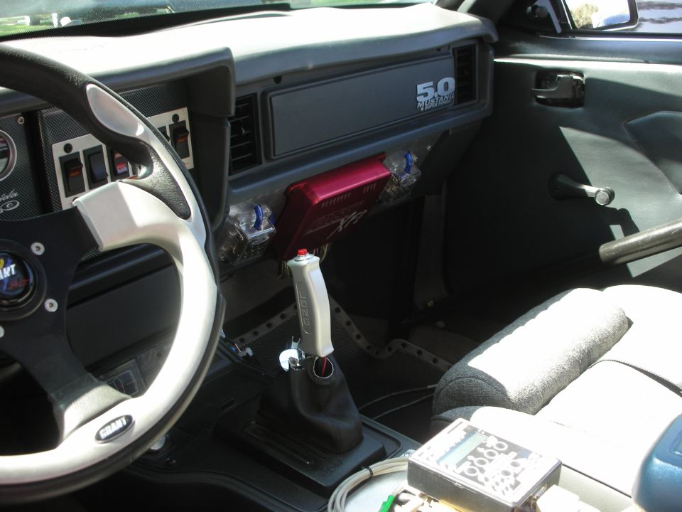 Interior of a car with a Grant steering wheel, 5.0 Mustang dashboard badge, and aftermarket shifter