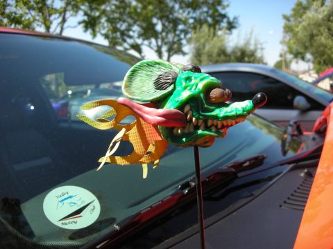 1998 Ford Crown Victoria - A custom green rat rod ornament is mounted on the hood of a car, with another vehicle visible in the background.