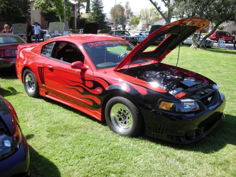 1998 Ford Crown Victoria - A customized Ford Mustang is displayed with its hood open at an outdoor car show.